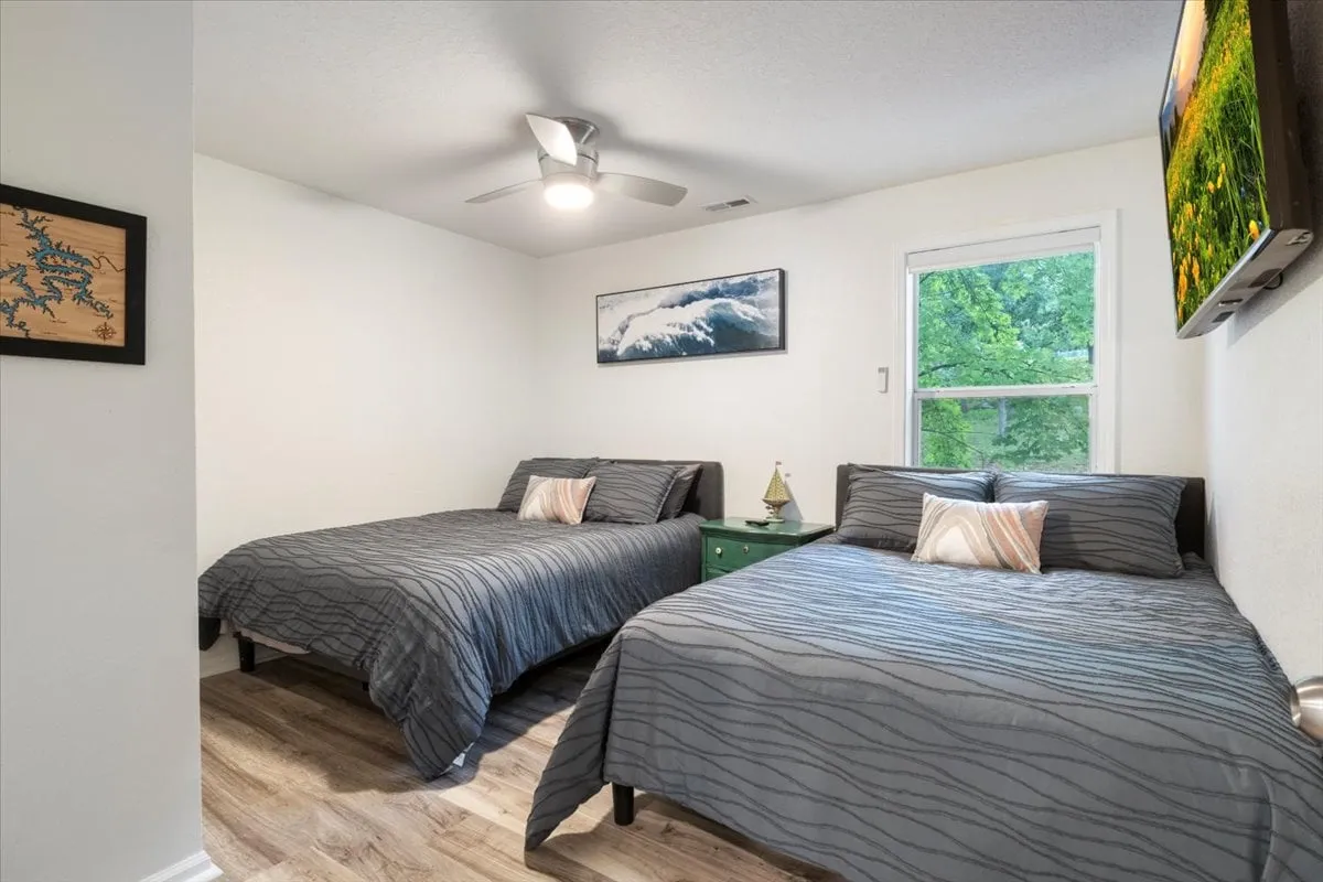 A comfortable bedroom with two beds, a green bedside table, attractive wall art, and a window letting in plenty of natural light. The setup is ideal for families or groups seeking flexible sleeping arrangements.