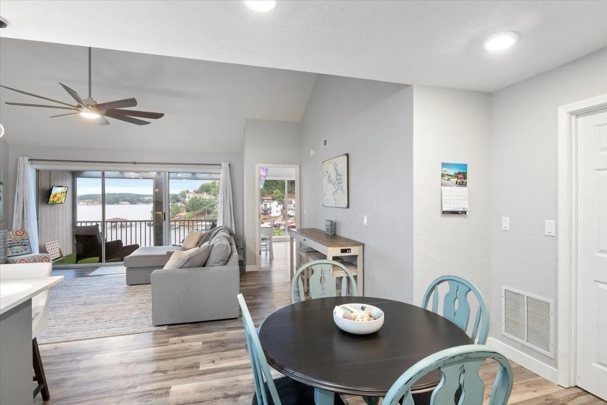 A bright, cozy space blending the dining area, sofa with colorful cushions, and large windows framing sweeping lake views. The combination of comfortable seating and an inviting table creates a perfect spot for game nights, meals, and socializing, all with the lake as a backdrop.