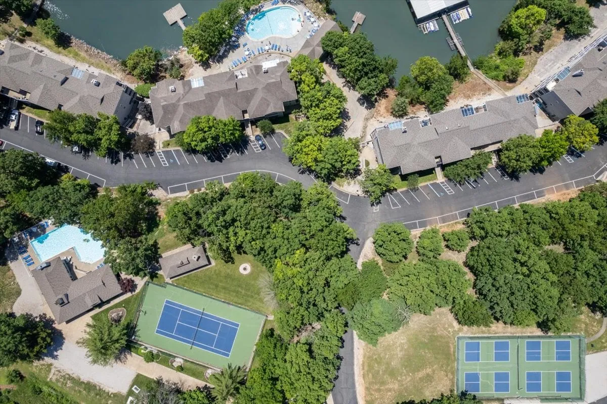 A wide exterior view showcasing swimming pools, a tennis court, lush greenery, and the waterway—offering multiple recreational options in one shot.