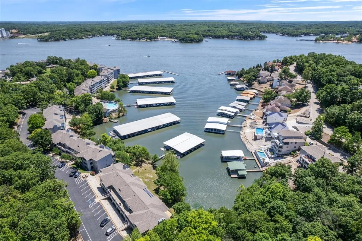 A serene view of the marina with multiple boats, lush surrounding greenery, waterfront homes, and boathouses. Activities like boating, fishing, and sunbathing are suggested, capturing lakeside adventure and relaxation.