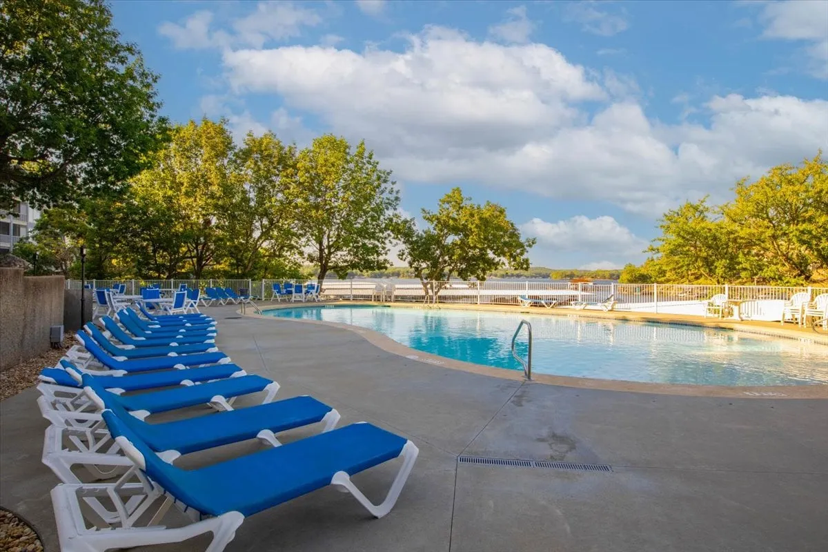 A relaxed poolside scene with a sparkling swimming pool, lounge chairs, and trees, all with a beautiful water view in the background. The setup suggests both leisure and opportunities for breaks outdoors.