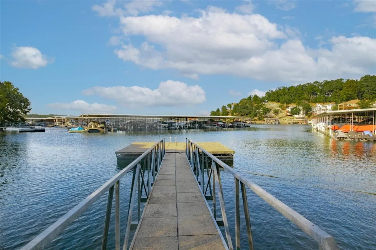 This exterior shot features a dock with several boats moored, calm water, and hillside homes in the background. The scene evokes peaceful moments by the water and offers a clear view of boating access, highlighting the lakeside lifestyle central to Soul Star Sunset.
