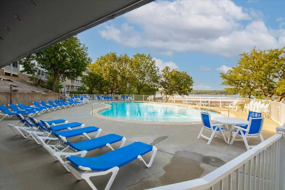 This exterior shot captures a sun-soaked pool area with lounge chairs and an outdoor table, surrounded by lush trees. The inviting space is perfect for swimming, sunbathing, and socializing with friends throughout the day or into the evening.