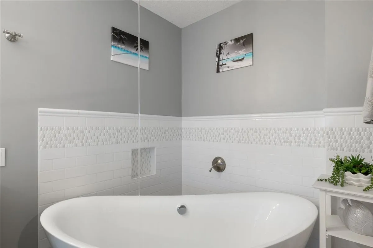 A luxurious bathroom with a deep freestanding bathtub, calming wall art, textured tile work, and a thoughtful plant arrangement. The space evokes a spa-like atmosphere for self-care and relaxation.