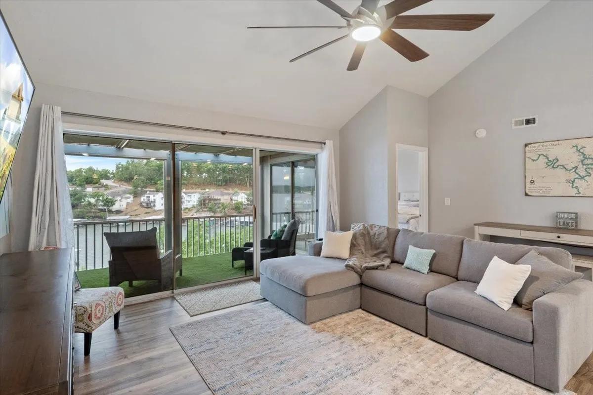 A spacious living area featuring a large sectional sofa facing a television, with sliding glass doors that open onto a balcony. The setup is ideal for movie nights or cozy relaxation after a day by the lake, seamlessly blending indoor comfort with access to outdoor views.