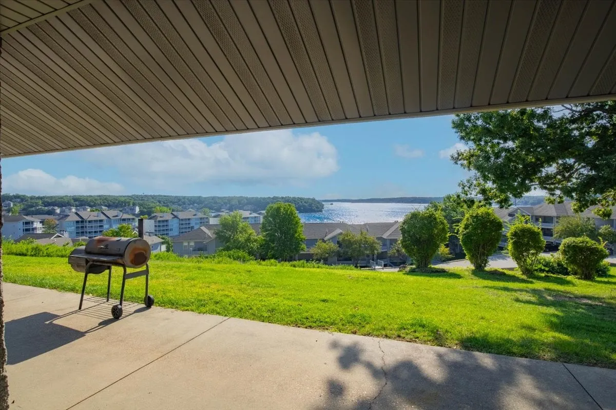 This exterior image features a well-kept lawn with grill, outdoor seating, and a stunning water view framed by trees. The setting is ideal for relaxed barbecues, sunset dinners, and evening socializing, as well as quiet mornings with coffee overlooking the lake.
