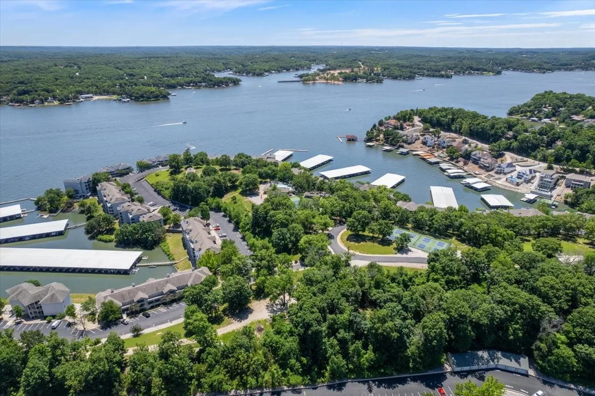 A broad exterior shot featuring the lake, marina, lush greenery, and residential buildings. The scene is tranquil and expansive, showcasing multiple trails and open areas ideal for walking pets and exploring the lakeside environment.